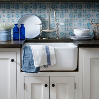 Close up of a butler sink in a Shaker kitchen with blue geo tiles on the wall