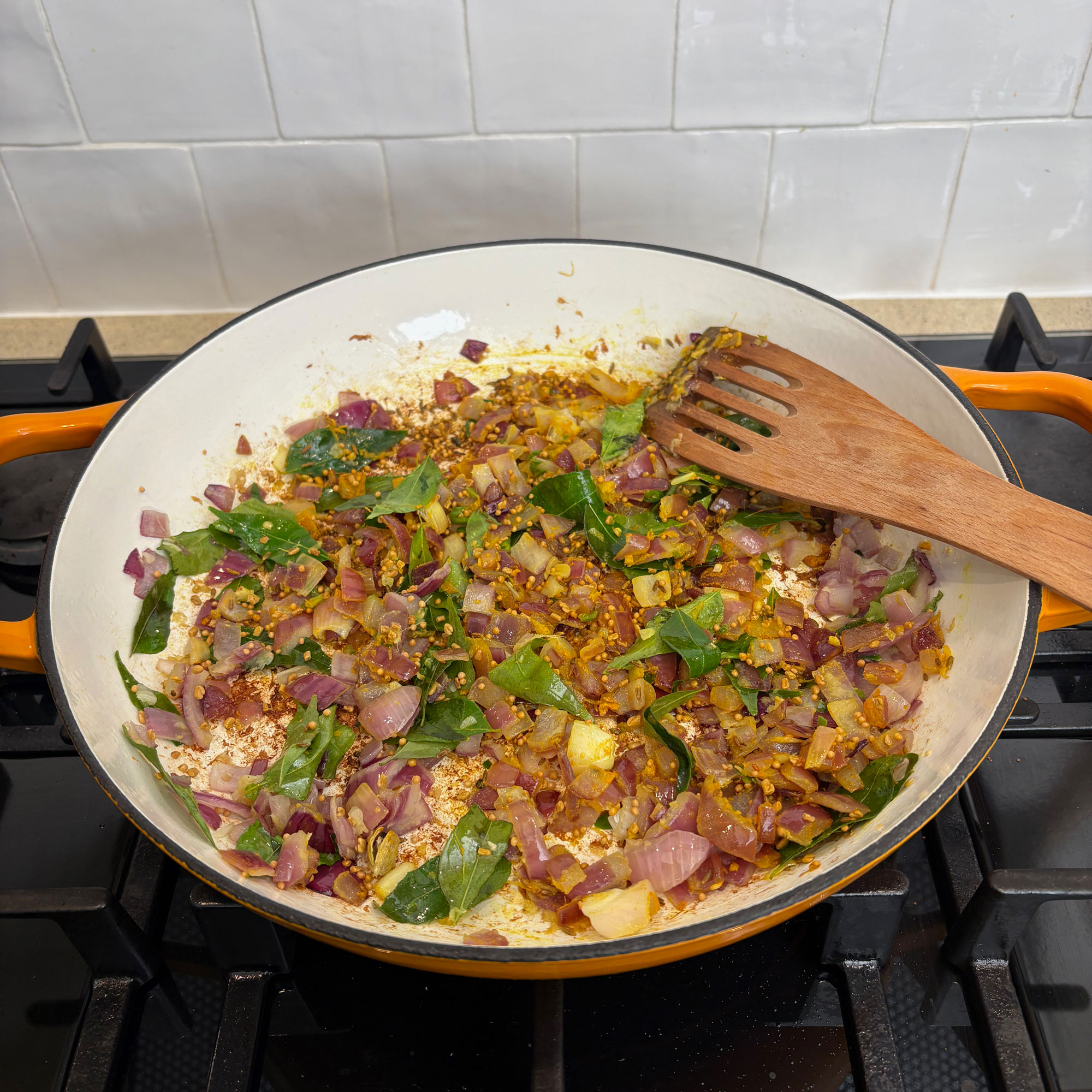 Orange cast iron pan on black hob with pepper and onion mix