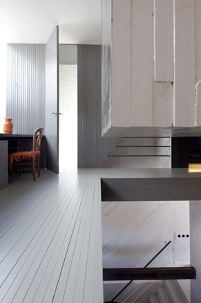 Grey walls and floor with vertical design lines. On the left is a black table with a wooden chair in orange seat