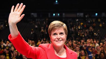 Nicola Sturgeon in red suit in front of a crowd of people, waving