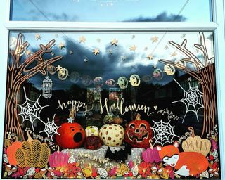 Halloween window decor with painted pumpkin, fox, cobweb and tree autumnal design with carved and decorated pumpkins in display, gold foil pumpkin bunting and LED fairy style lights