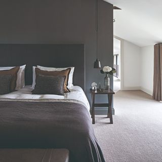 A bedroom with a grey carpet, an anthracite wall behind a black bed with black and white bed linen