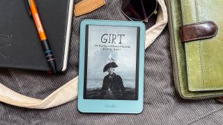 A book cover displayed on the Amazon Kindle 2026 while it lies on a cloth bag and surrounded by handbag contents