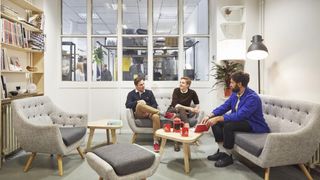 Three people drink tea and chat in relaxed breakout area