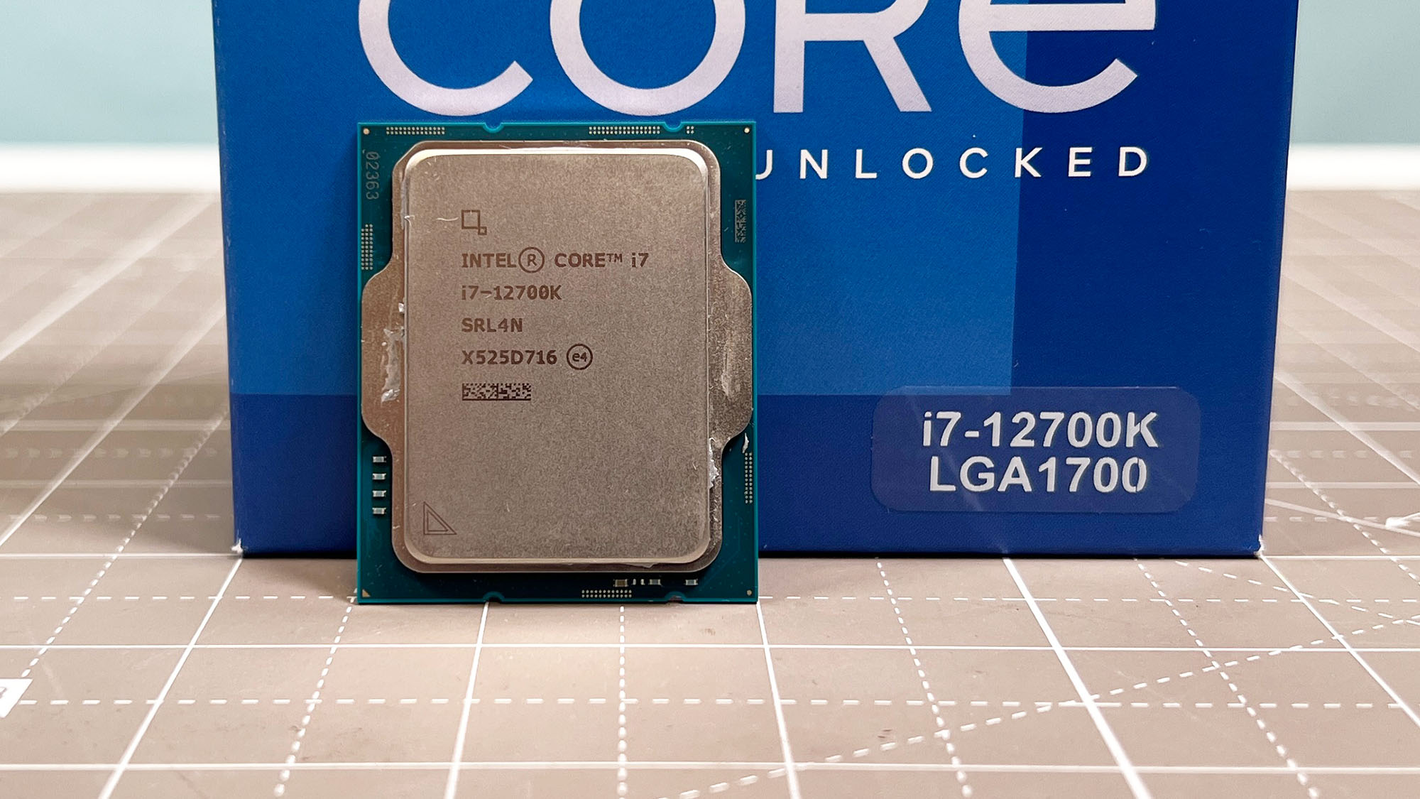 An Intel Core i7-12700K standing upright on a table next to its retail packaging