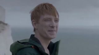 Domhnall Gleeson smiling on a cliff by the sea in Black Mirror