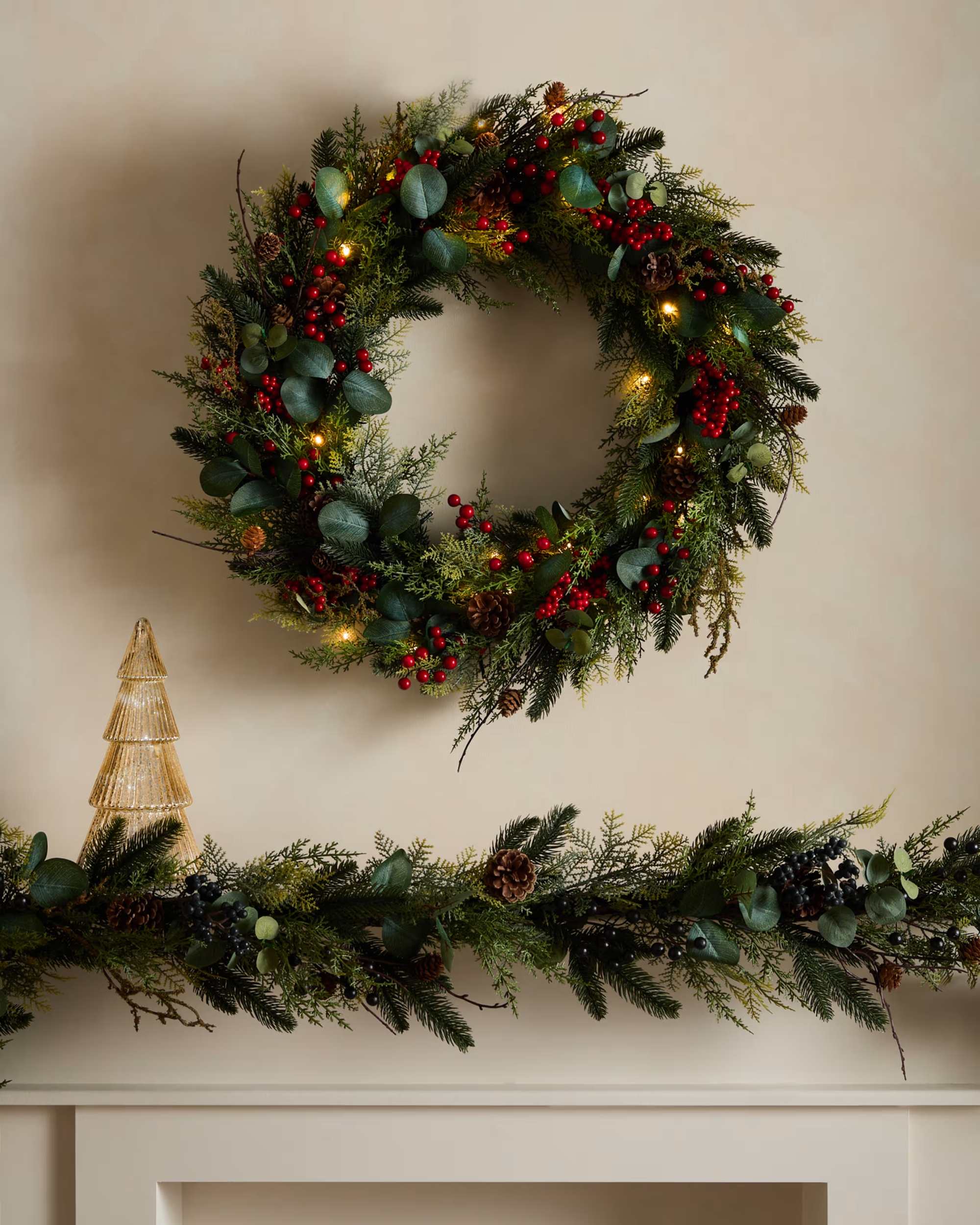 A red and green, traditional Christmas wreath hanging over a mantel that has matching garland on it.
