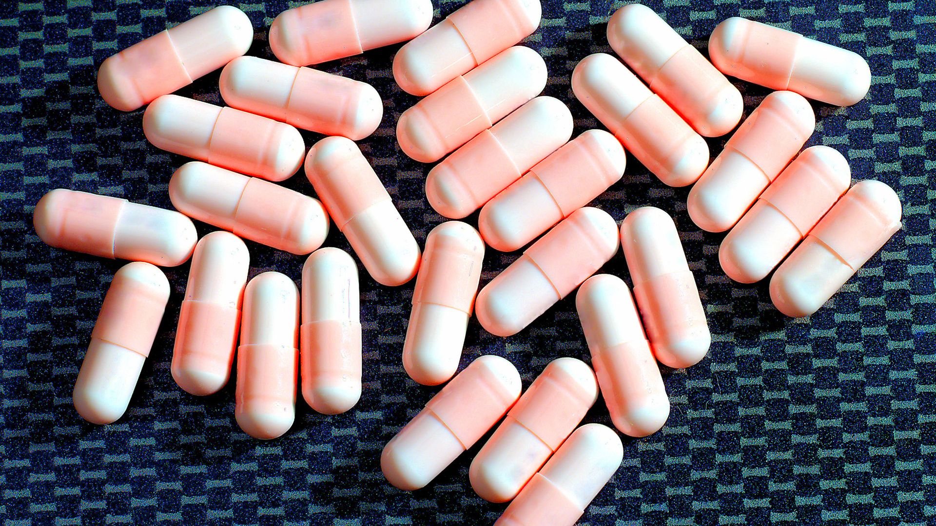 A handful of pink pills against a blue background.