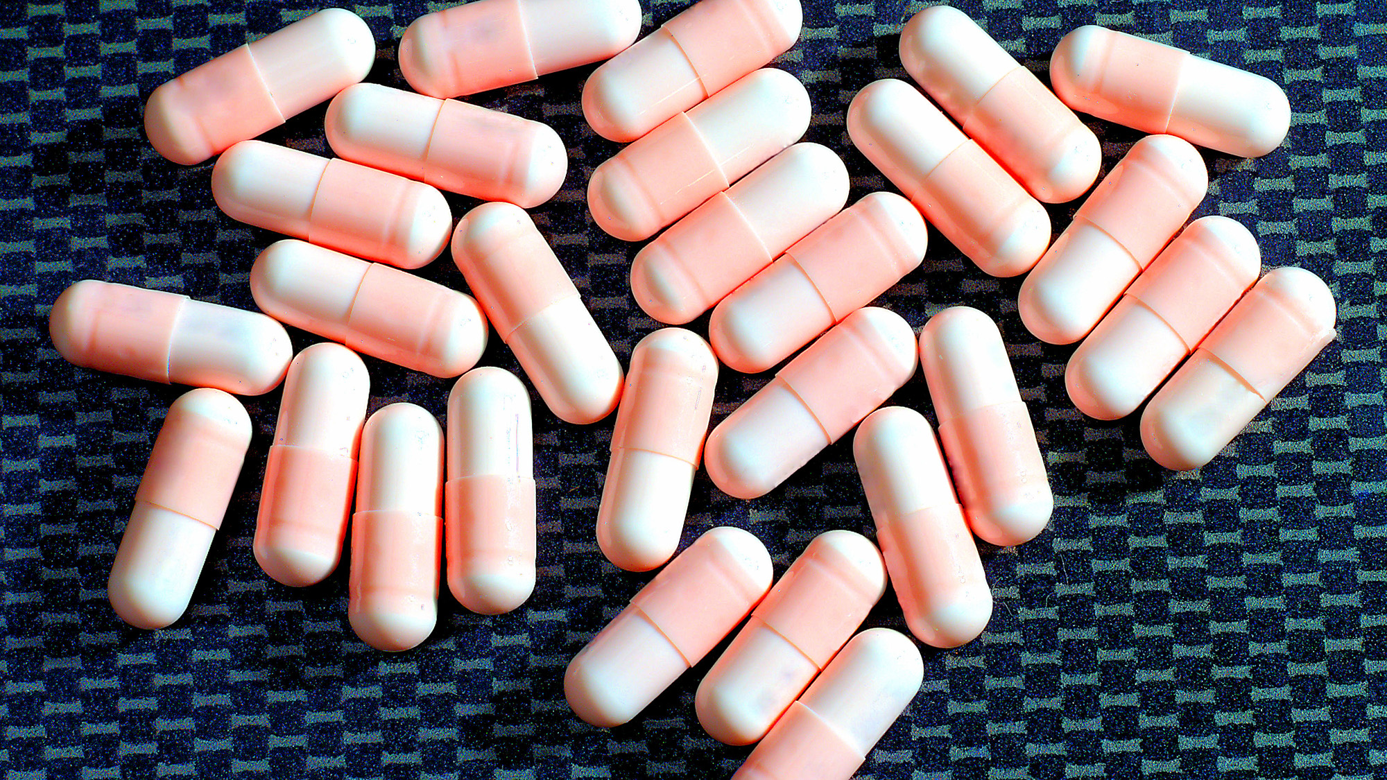 A handful of pink pills against a blue background.
