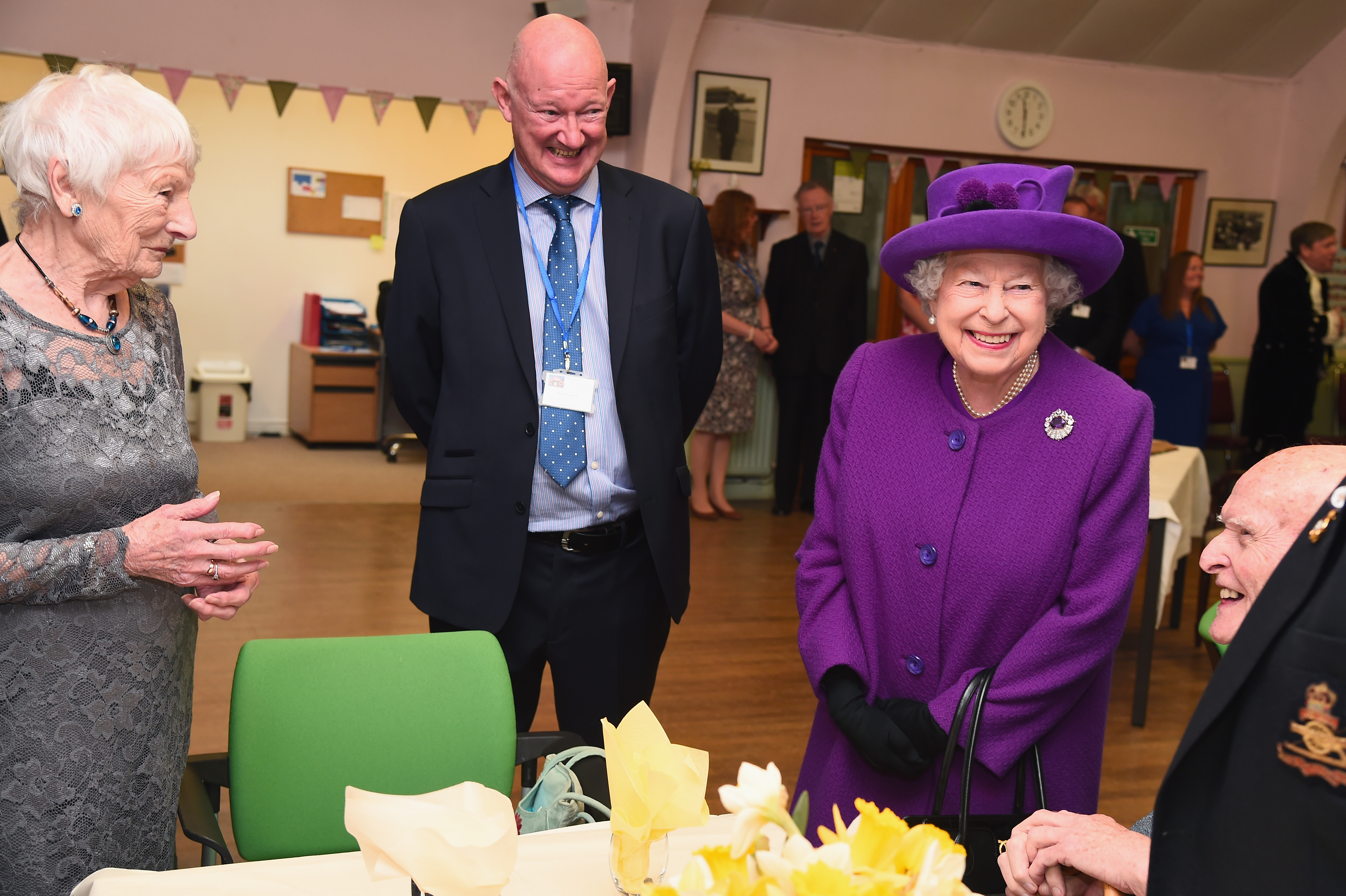 Queen Elizabeth laughing in a purple coat and hat standing with senior citizens