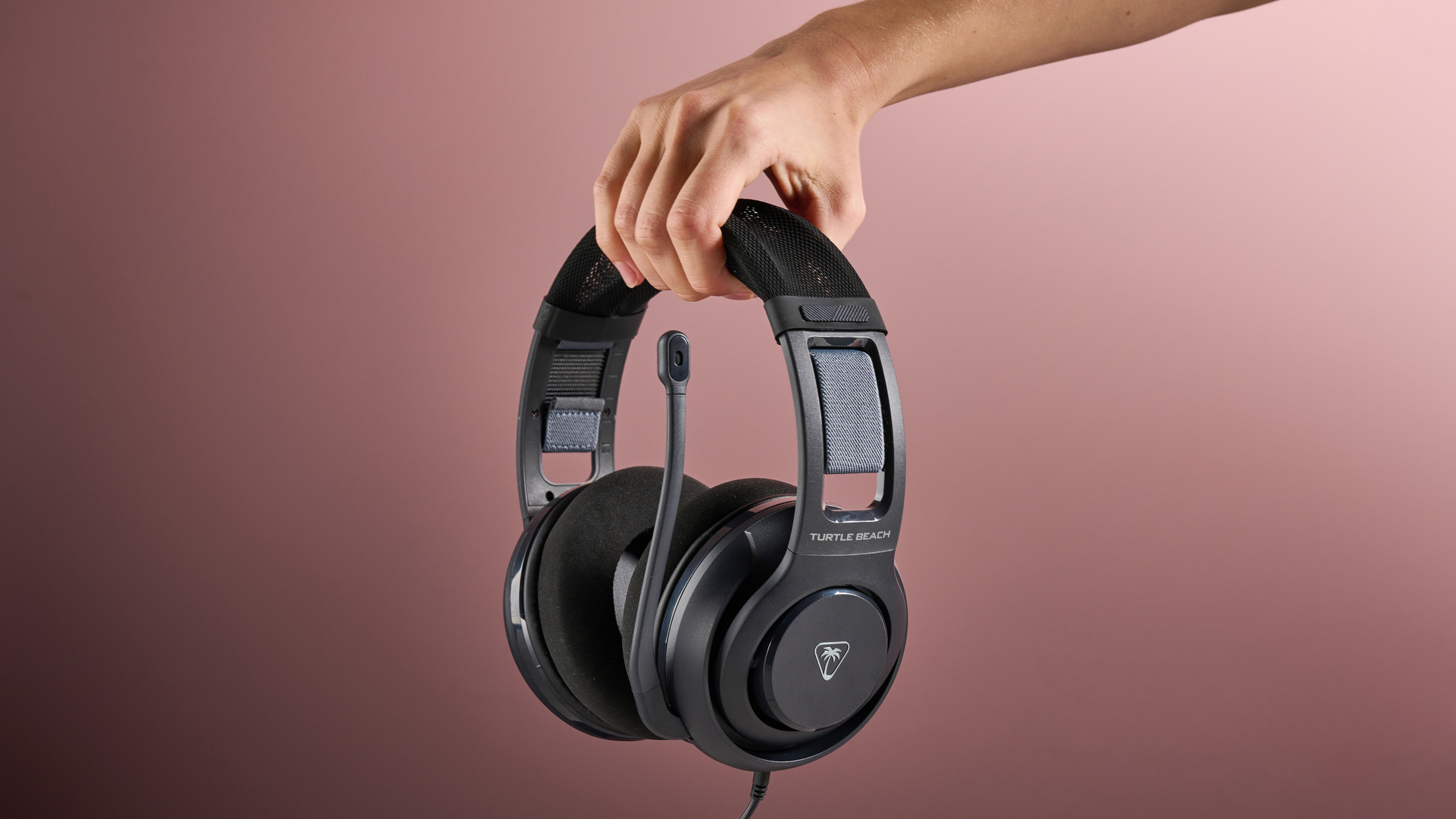 A hand holds the Turtle Beach Atlas 200 in front of a pink background.