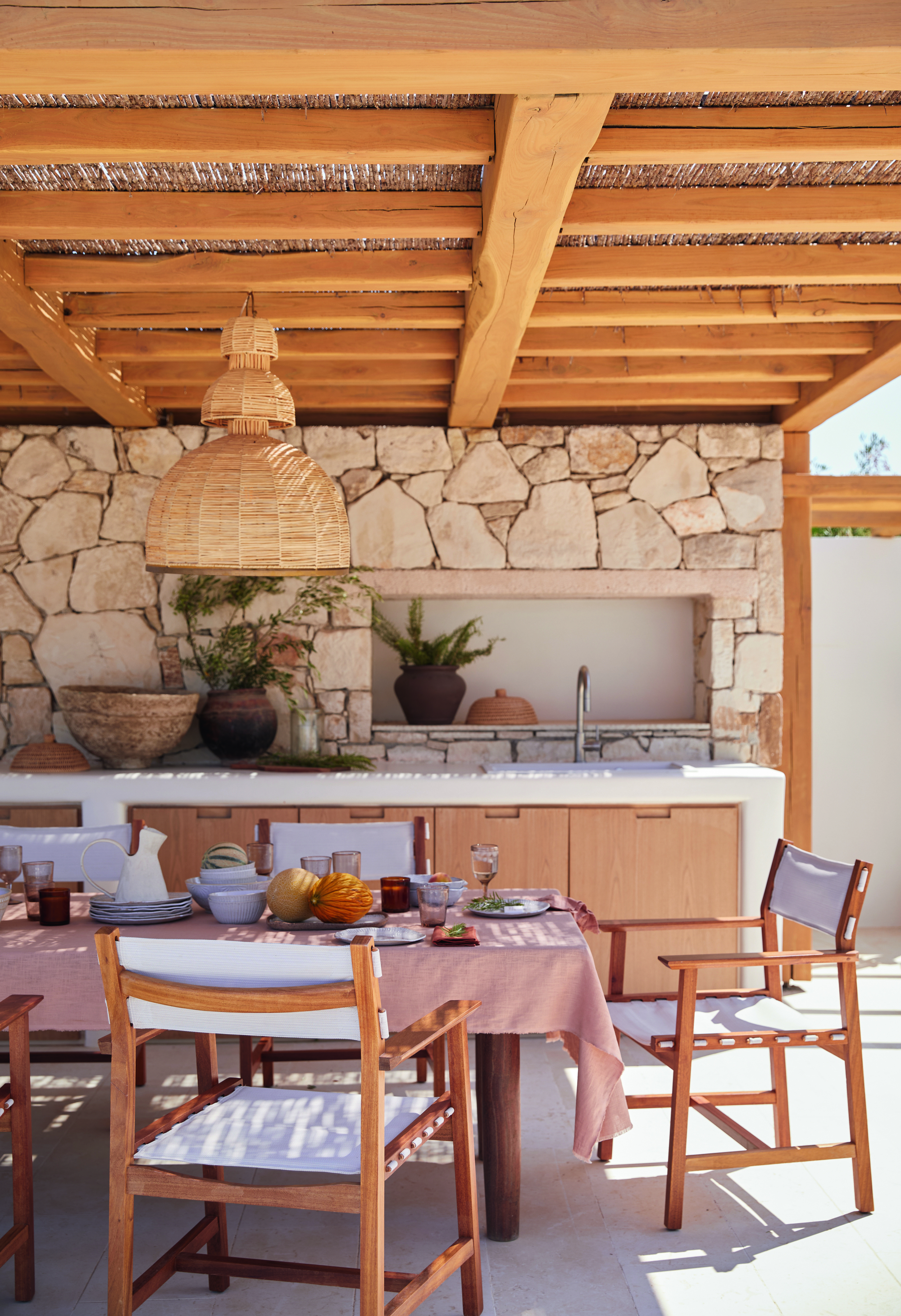 An outdoor terrace with a dining table and outdoor kitchen sheltered under a pergola