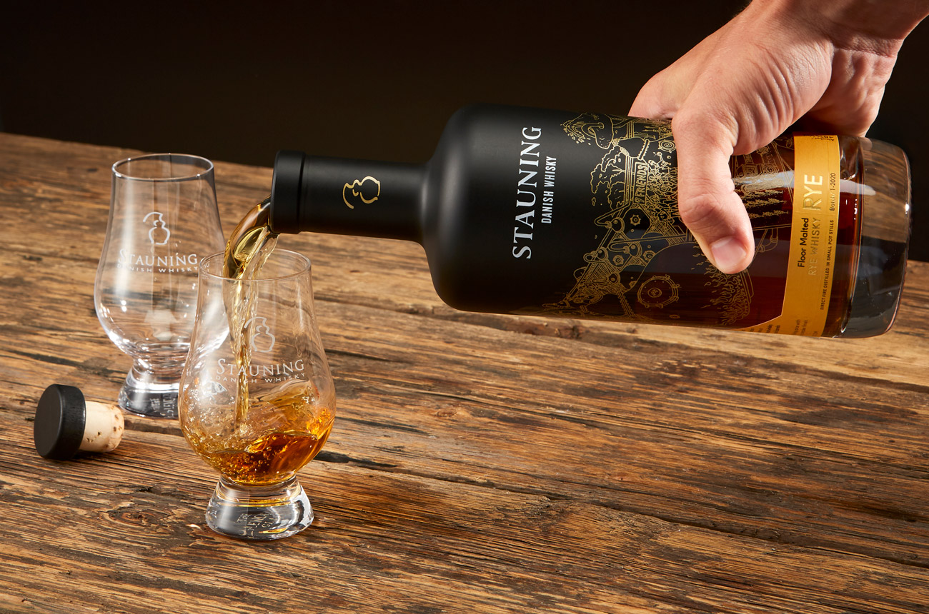 Hand pours a bottle of whisky into two glasses