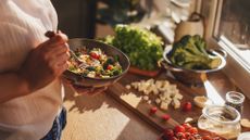 MIND diet components, including green vegetables and eggs in a bowl held by a woman with ingredients on wooden chopping board on counter in kitchen