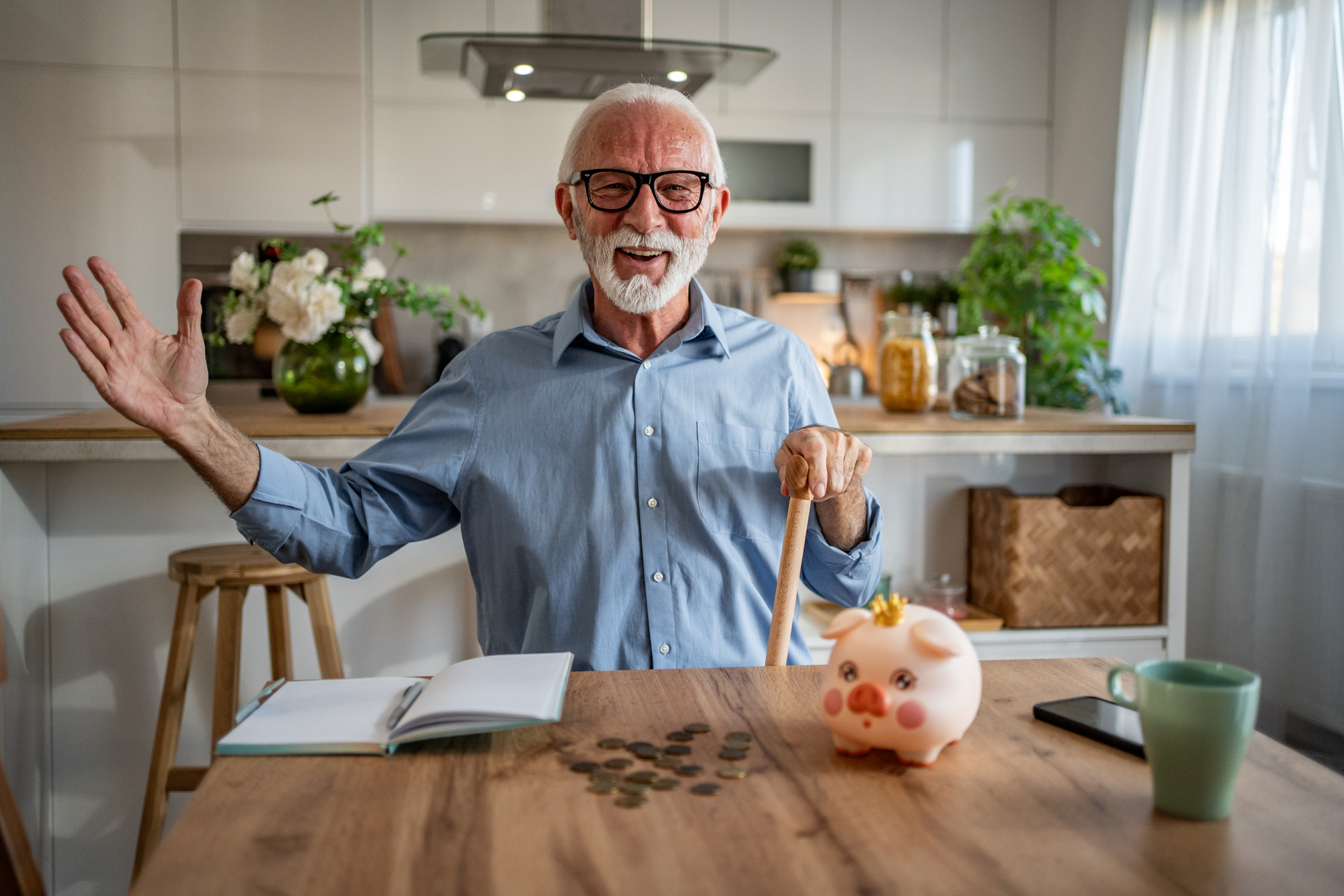 Older man in kitchen with piggy bank and coins on counter.