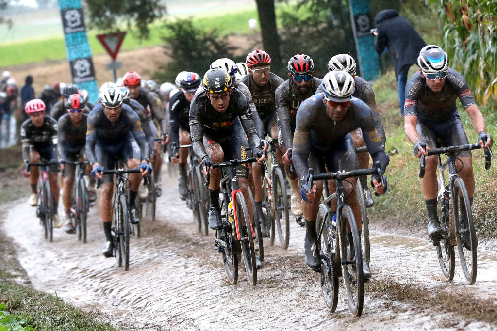 El pelotón, cubierto de barro y mojado, rueda sobre un sector de adoquines embarrados y resbaladizos durante la París-Roubaix 2021