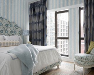 blue bedroom with blue floral bed, patterned wallpaper and dark blue curtains