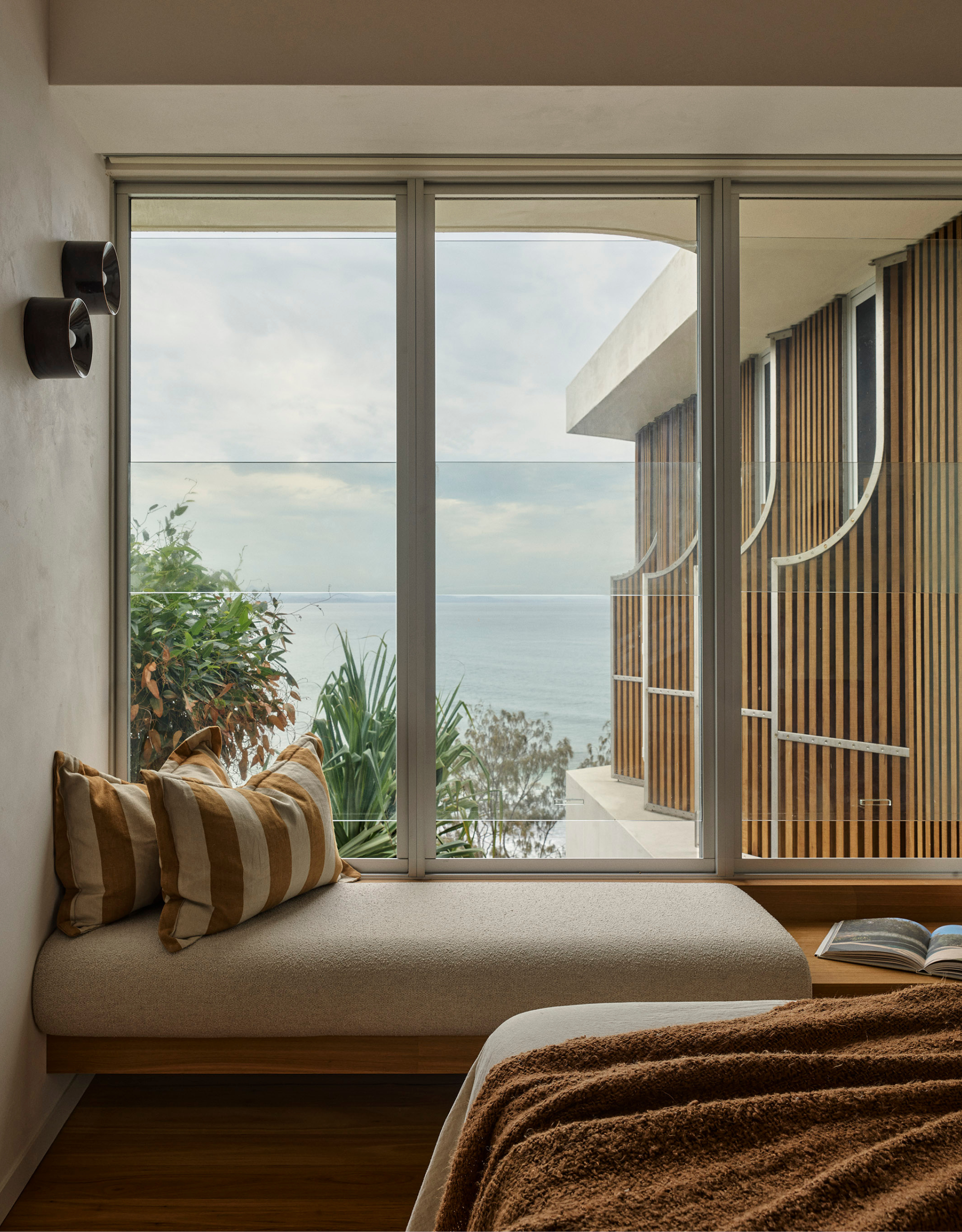 A bedroom with a floating sofa bench with striped pillows by large glass windows