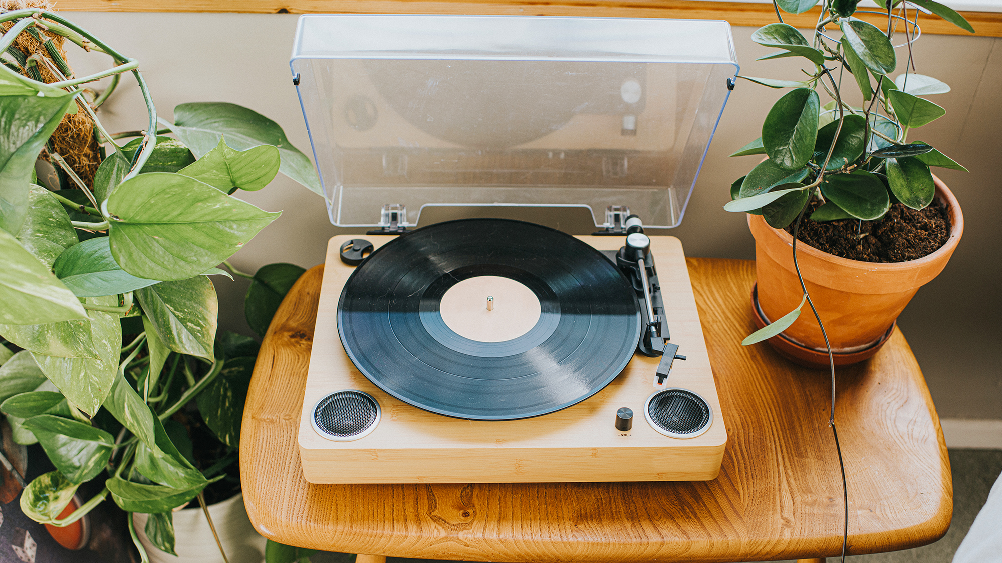 Elevated view of a modern record player on a wooden table. A potted plant sits to one side.