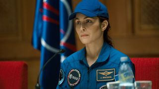 a woman in a blue astronaut uniform sits at a desk