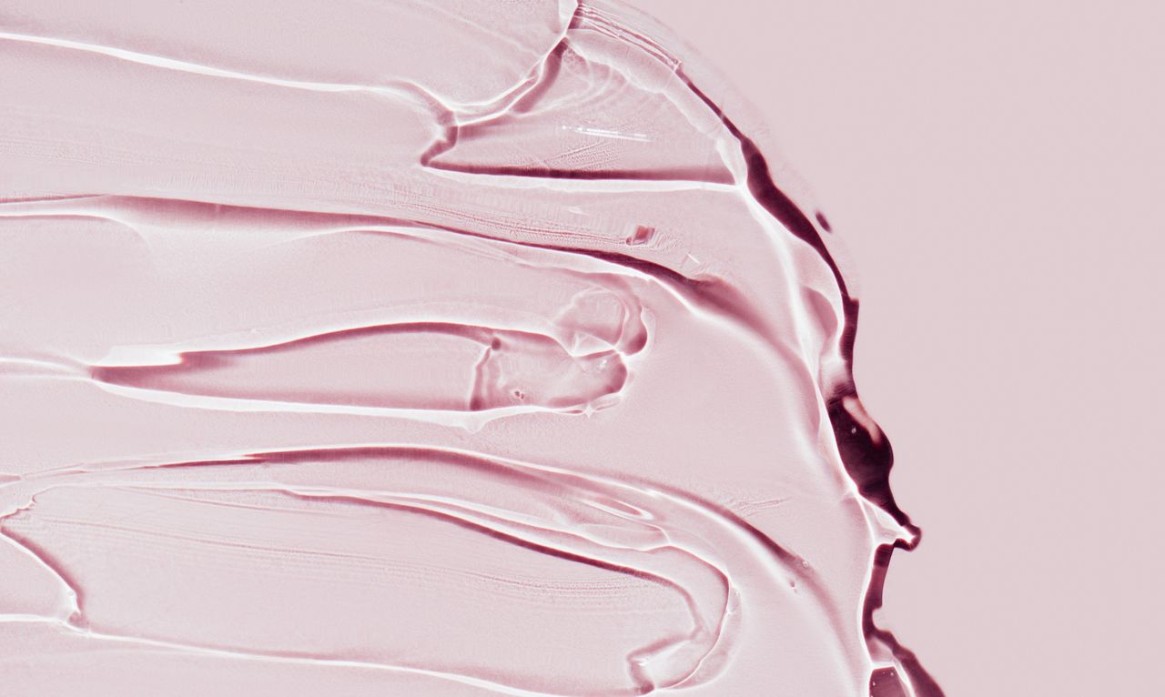 Closeup strokes of transparent cosmetic gel for spa procedure spread on bright pink background. Serum or antibacterial gel are the main products of the year