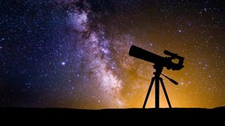 A low black horizon gives way to the rise of the milky way in the night sky, glowing on the left in hues of blue, and hues of orange on the right, which break for the silhouette of a telescope on a tripod, pointing left.