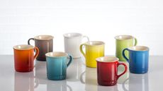Le Creuset stoneware mugs in different colors on a countertop