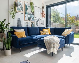 Blue Snug sofa with yellow cushions in white living room in from of glass sliding doors