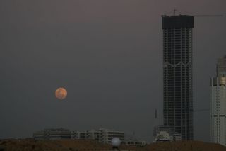 a reddish full moon seen through dusty clouds