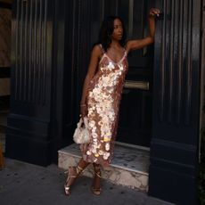 Woman leaning against a wall wearing a sequined J. Crew dress with a evening bag