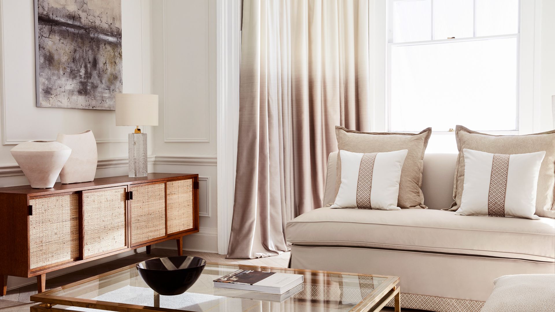 neutral Japandi living room with beige cushioned sofas black wooden console and abstract artwork on walls