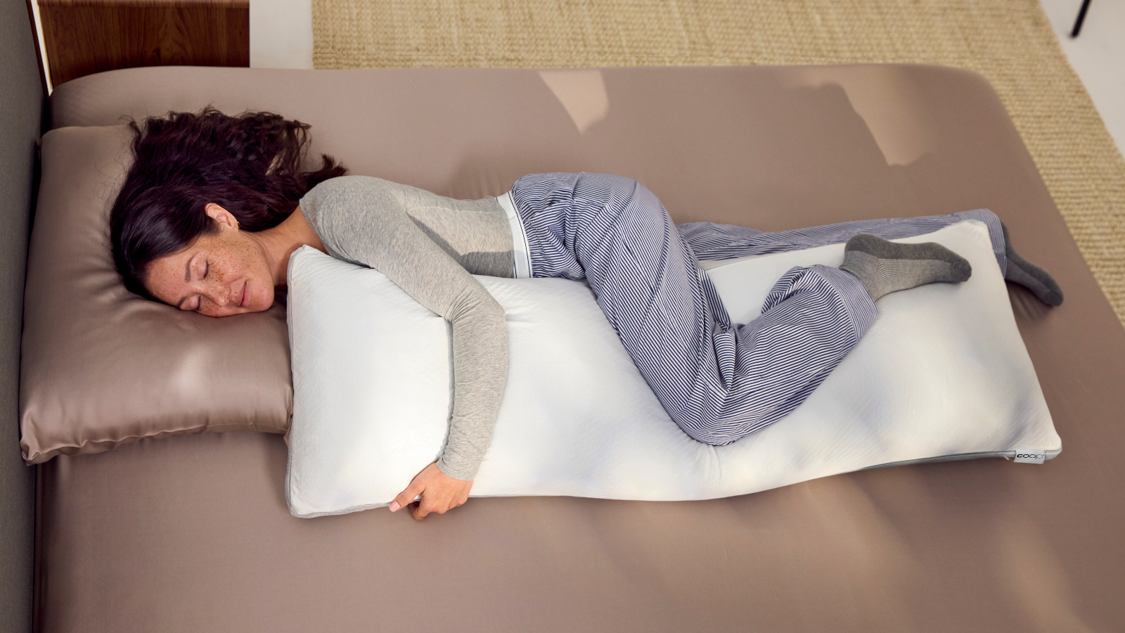 Woman sleeping in bed hugging a white body pillow that's part of the new Coop Cool+ range