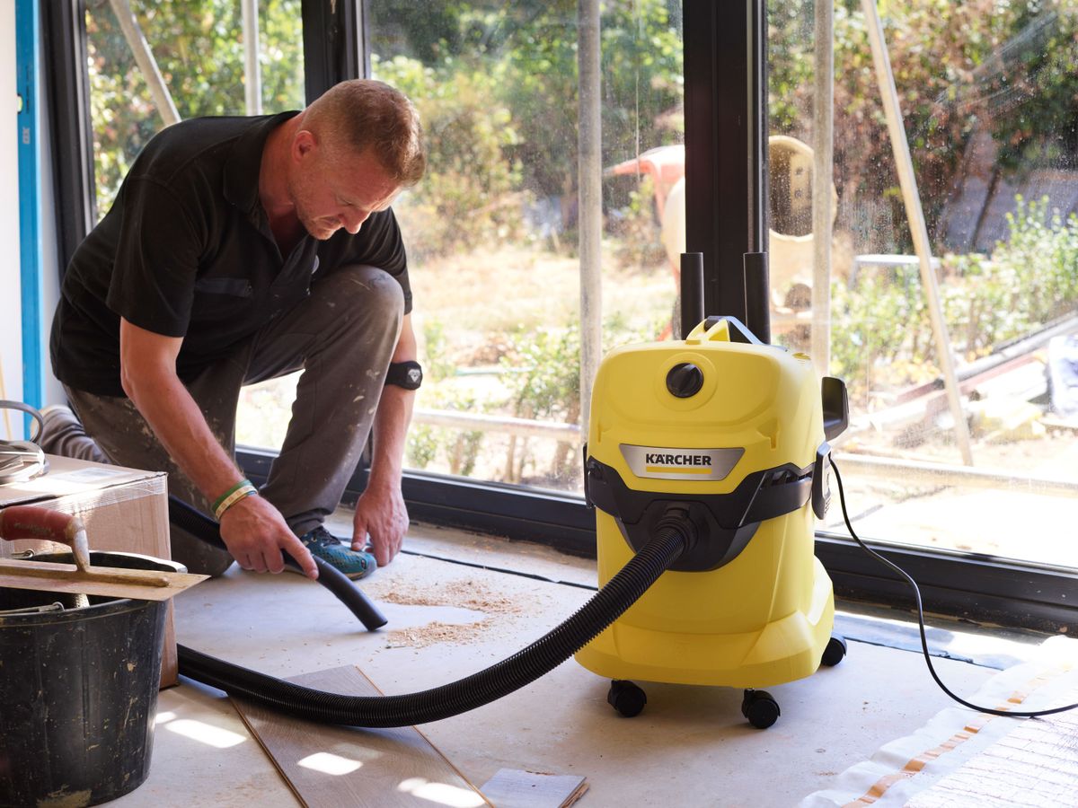 A man uses a Kärcher WD 4 to suck up dust from a floor on a building site