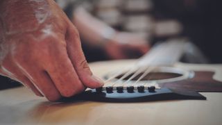 Man presses acoustic bridge pin into an acoustic guitar