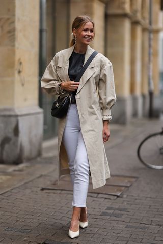 A woman wearing white jeans and a beige trench coat