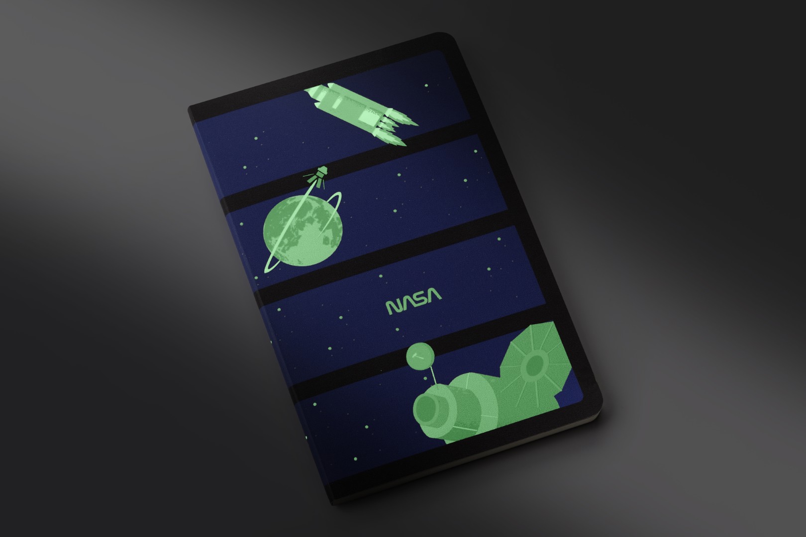 Softcover, glowing-in-the-dark Volant Journal from the collection of NASA-inspired Limited Edition Notebooks from Moleskine. There are four dark blue panels in a column, each with it's own grayscale image that is glowing in the dark. From top to bottom: rocket, Earth with orbiting satellite, NASA text, big satellite.