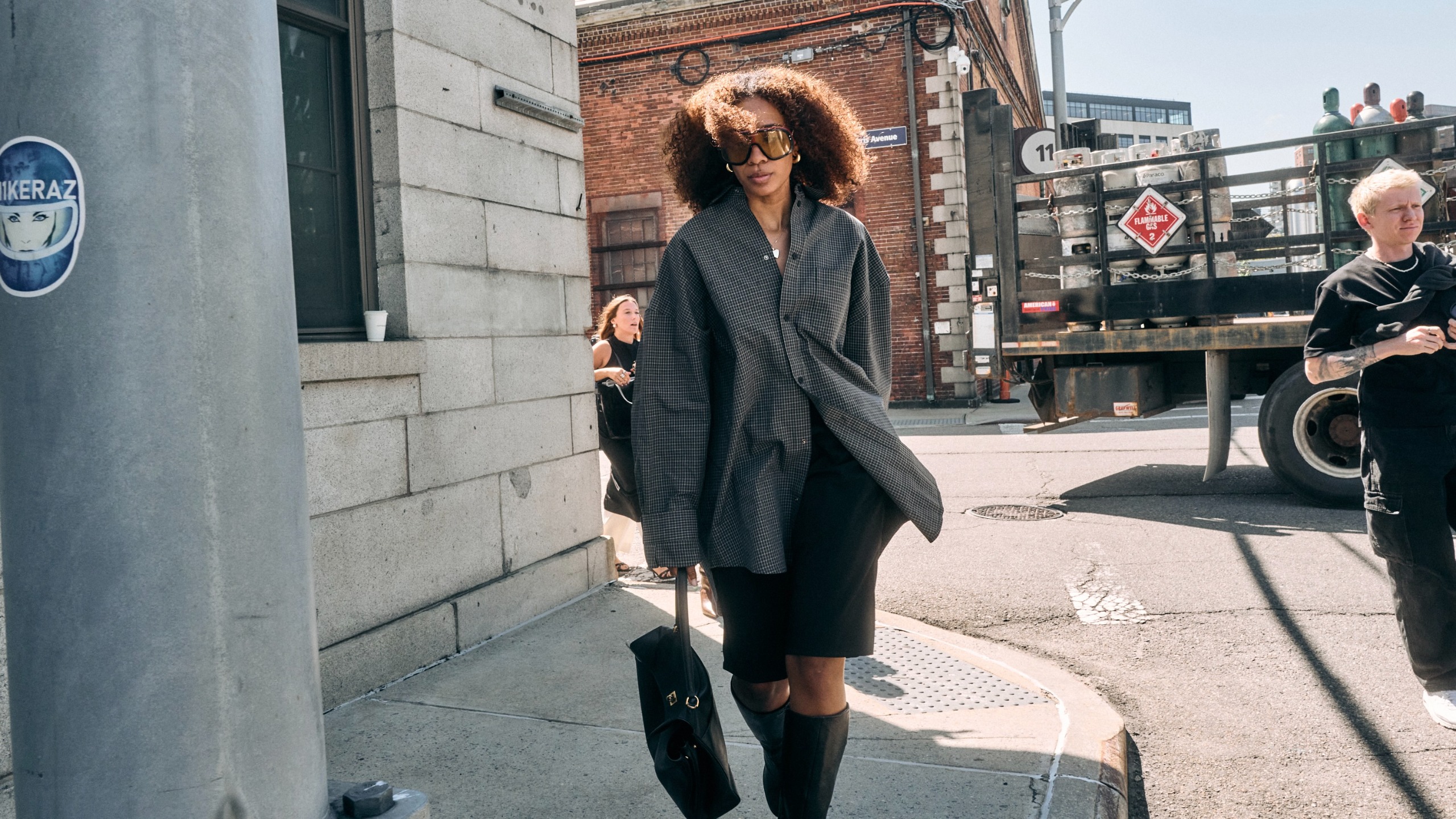 Chic woman street style wearing oversized sunglasses with an oversized button down top, black knee-length shorts and knee high boots with a black bag 