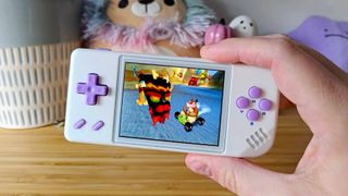 Hand holding Anbernic RG28XX handheld with Crash Team Racing PS1 gameplay on screen.