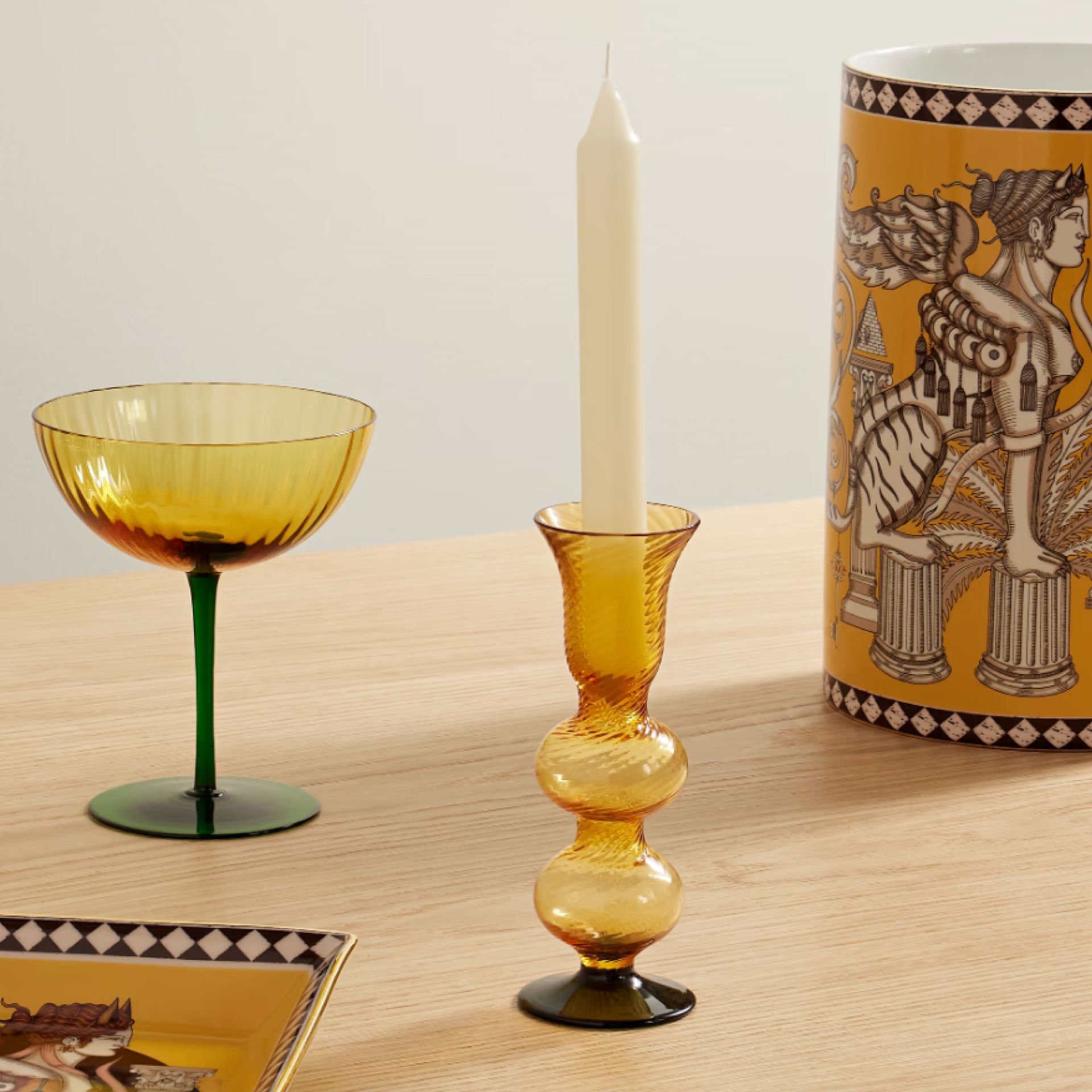 A yellow glass candlestick image with a glass and candle in the background