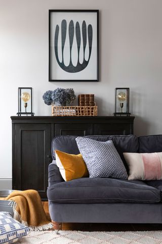 Pale living room with grey sofa, a black sideboard and black accents as well as yellow and blue accessories