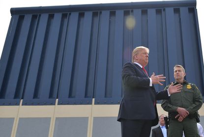 Donald Trump stands in front of a border wall prototype.