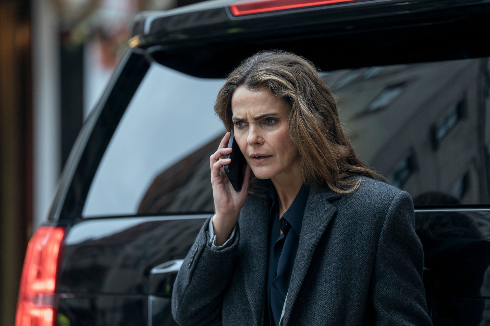 Keri Russell as Kate Wyler, holding a phone to her ear while standing behind a black SUV, in 'The Diplomat' season 4.