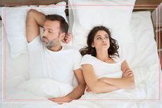 A couple lying in bed looking annoyed