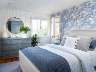 Bedroom with toile wallpaper, bed dressed in white and blue and wood floor