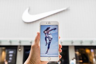 A hand holding a mobile with the Nike Training app in front of Nike store