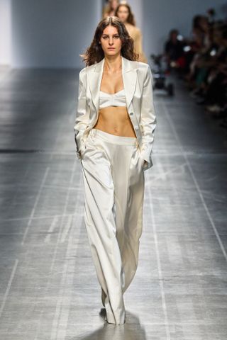 Spring Trouser Trends 2025: A model wears cream satin trousers on the Ermanno Scervino runway