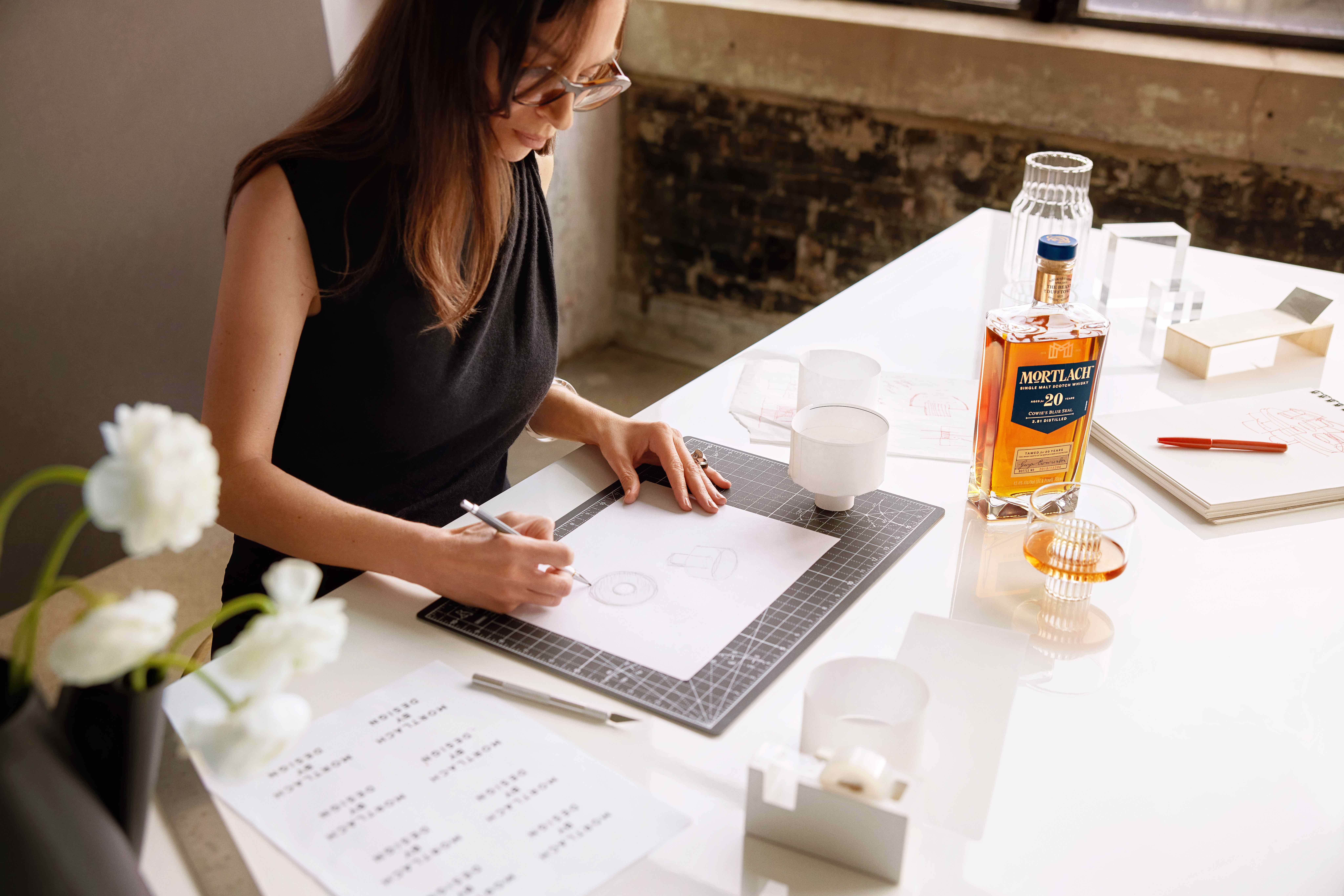 Designer Felicia Ferrone sketching, with Mortlach whisky and her glass designs on desk