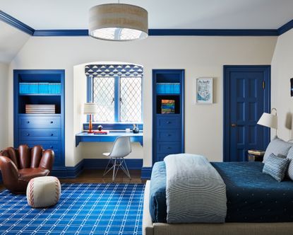 Bedroom ideas for boys with white walls, blue painted accents, a built-in blue desk in the alcove window and a chair shaped like a baseball mit
