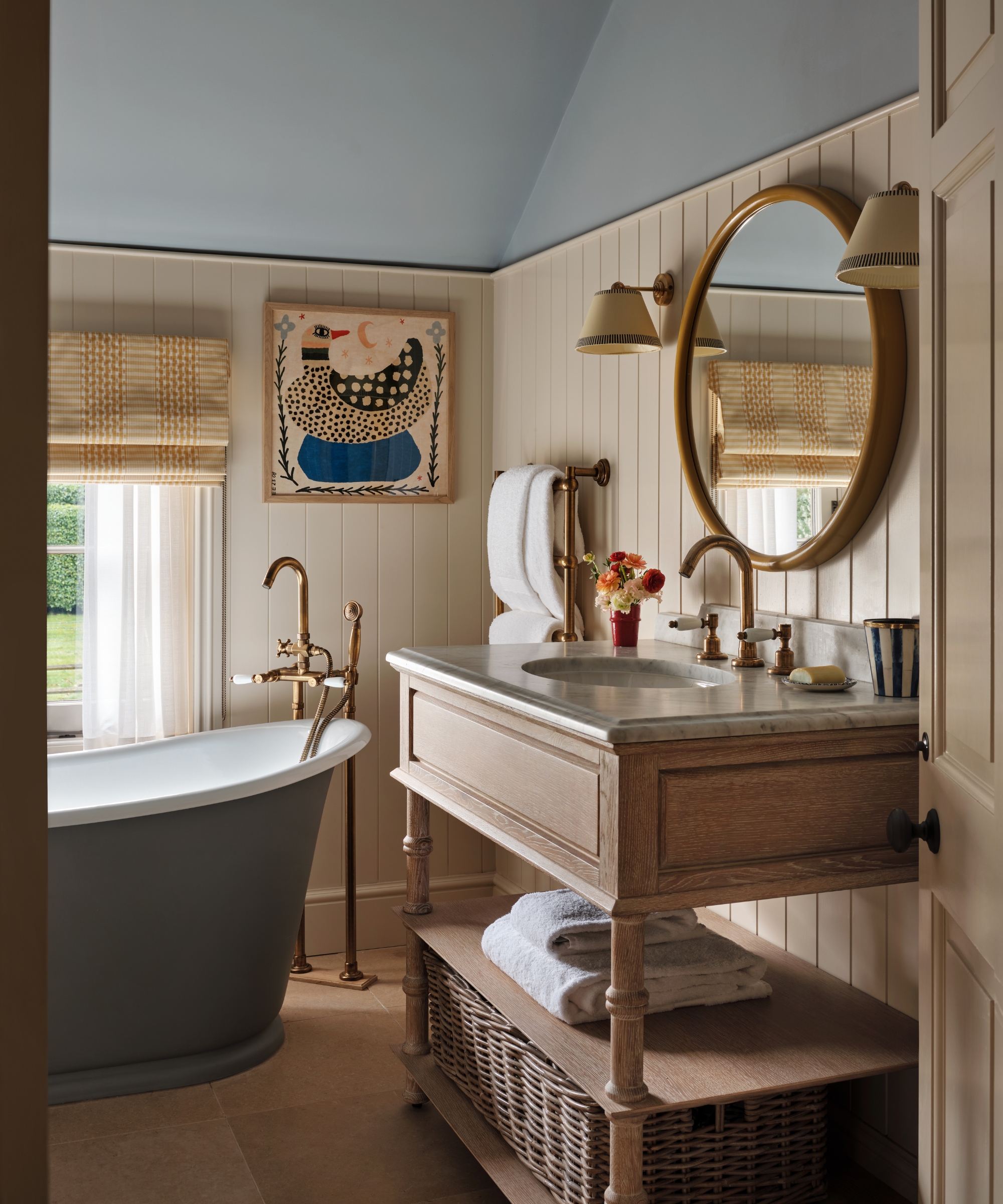 a country house bathroom with blue vaulted ceilings, cream paneled walls, and a wooden vanity