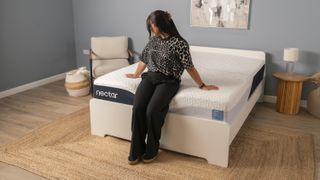A Tom's Guide sleep writer sat on the edge of the Nectar Classic in a clean, minimalist sleep studio